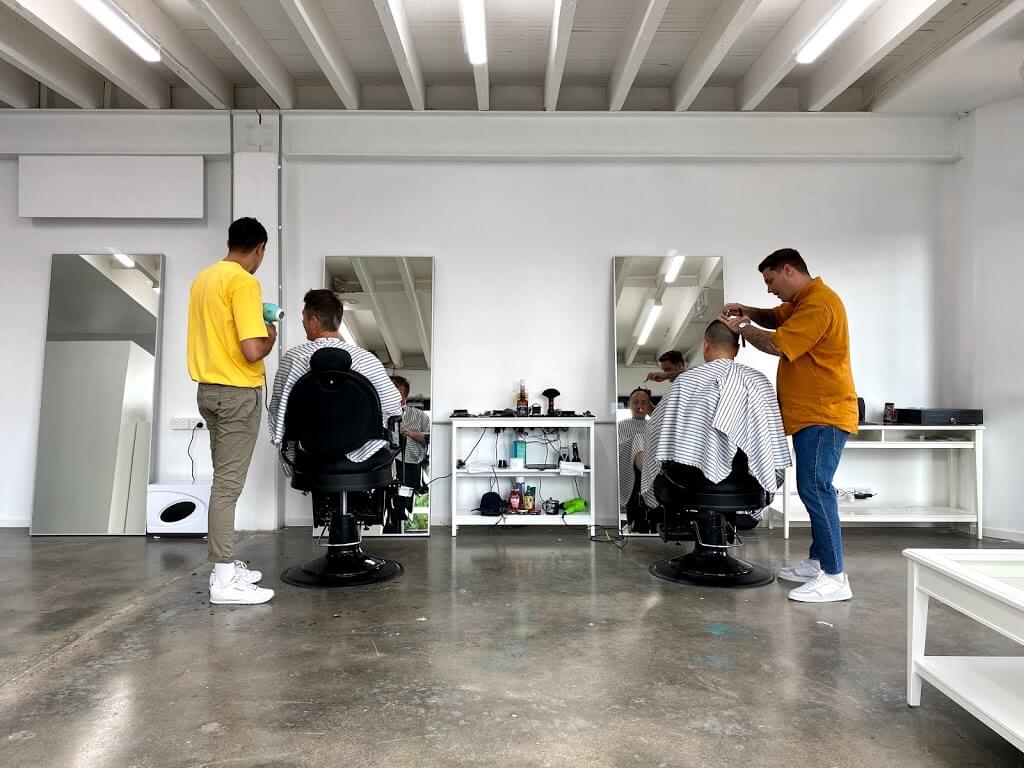 Two barbers cutting hair in the BOY Barbershop, a bright white room with mirrors and two black barber chairs.